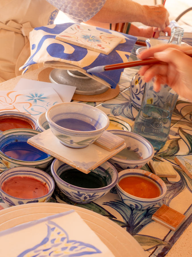 Person painting ceramic items on a table with various colors and tools.